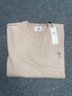 Beige stickad tröja från Ami -  KOM MED PRIS FÖRSLAG, ALDRIG ANVÄND!      Snygg beige stickad tröja från Ami Alexandre Mattiussi med rund hals och ribbade muddar. Tröjan har Ami-loggan broderad med hjärta på bröstet. Perfekt för dig som gillar stilrena och mjuka plagg med exklusiv känsla.