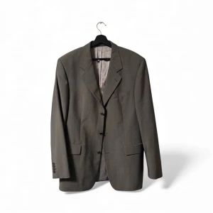 Grå kavaj från Hugo Boss - Snygg grå kavaj från Hugo Boss med klassisk passform och tre knappar framtill. Kavajen har breda slag, innerfoder i silke och två fickor med lock. Perfekt för dig som vill ha en stilren och tidlös look.