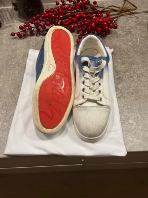 Christian Louboutin blåvita sneakers - Säljer ett par snygga sneakers från Christian Louboutin med vit och blå gradient på ovandelen, klassisk röd sula och rund tå. Skorna har snörning och är tillverkade i canvas och skinn. Perfekt för dig som gillar exklusiva och unika sneakers. Pris kan diskuteras!!