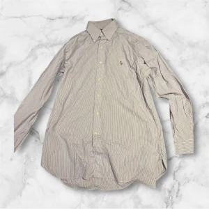 Randig Ralph Lauren shorta. - En väldigt fräsch och snygg randig raffe shorta med lila och vit. Väldigt bra skit och en tidlös design som passar i alla sammanhang. Passar M