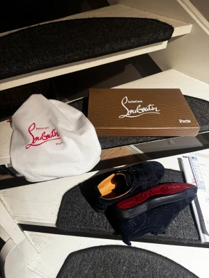 Christian Louboutin - Säljer ett par mörkblåa sneakers från Christian Louboutin i lyxig mocka med rund tå och snörning. Insidan är beige och sulan har den ikoniska röda Louboutin-loggan. Skorna kommer med originalkartong, dustbag och äkthetsbevis. Perfekt för dig som vill sticka ut med exklusiv stil.