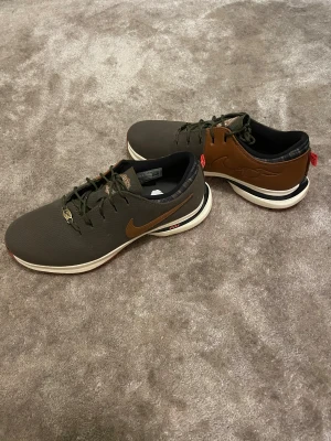Nike golfskor i olivgrönt och brunt - Nike golfskor med olivgrön textil och bruna skinnpaneler, vit och svart mellansula samt röd yttersula med svarta dobbar. Snygg snörning och diskret Nike-logga på sidan. Perfekt för dig som vill ha stil på golfbanan. Använda en gång på golfbanan och säljer då dessa har blivit för små. Hör av vid funderingar.🙌