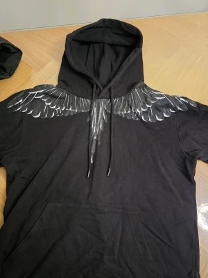 Marcelo Burlon - Svart hoodie från Marcelo Burlon County of Milan med ikoniskt vingtryck i grå och vitt över axlarna, både fram och bak. Med QR-scan🚀