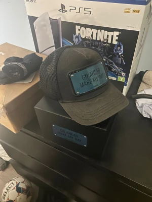 Svart keps John Hatter & Co - Snygg svart keps från John Hatter & Co med mesh på sidorna och bak. Framtill sitter en metallplatta med texten 'GO AHEAD MAKE MY DAY'. Kepsen har böjd skärm och justerbar passform. Levereras i originalförpackning med dustbag.