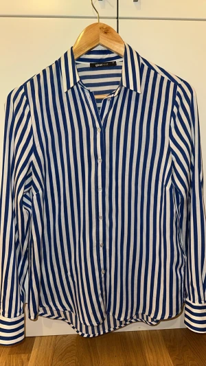 Blåvit randig skjorta Gina Tricot - Snygg skjorta från Gina Tricot i blåvitt randigt mönster. Klassisk krage, långa ärmar med manschett och knäppning framtill. Skjortan är i tunn bomull, perfekt för en fräsch och stilren look.