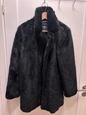 Svart pälsjacka (fuskpäls) från ONLY, strl M - Säljer en svart pälsjacka från ONLY i storlek M. Jackan har en fluffig och mjuk yta, hög krage och raka långa ärmar. Perfekt för dig som vill ha en cool och varm look under höst och vinter. Jackan är helsvart och har en klassisk, rak passform.