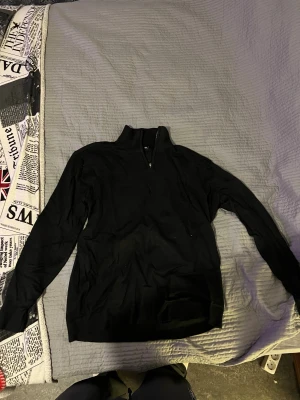 Svart half zip stickad tröja 157 - Svart stickad tröja från 157 med half zip och hög krage. Tröjan har långärmade ärmar och ribbade muddar vid hals, ärmslut och nederkant. Perfekt för dig som gillar enkel och stilren look med lite sportig touch.