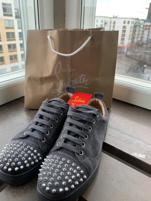 Grå mocka sneakers från Louboutin - Säljer ett par gråa sneakers från Christian Louboutin i mocka med ikoniska röda sulor, allt i bilden ingår 