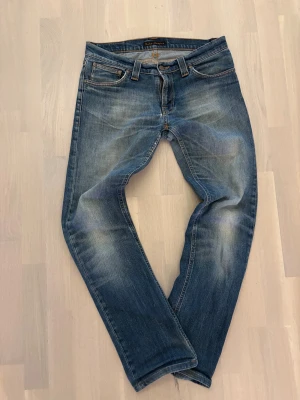 Vintage Nudie jeans - Snygga blå jeans från Nudie Jeans med klassisk femficksdesign och orangea sömmar på bakfickorna. Jeansen har en normal passform och är tillverkade i slitstarkt denim med lätt tvättad look. Perfekt för dig som gillar en avslappnad stil.