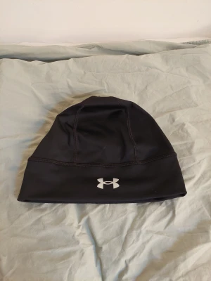 Svart Under Armour Storm mössa - Sportig svart mössa från Under Armour med Storm-logga på baksidan och klassiska UA-loggan på framsidan. Den är i nyskick och har bara använts ett fåtalgånger. Ordinariepriset var runt 300 kr