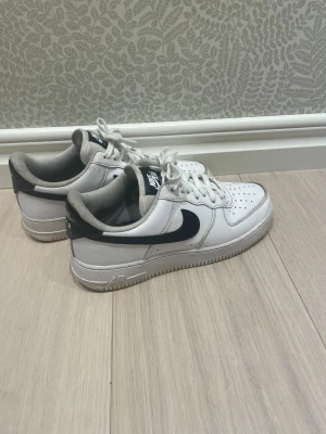 Nike Air Force 1 vita och svarta sneakers - Klassiska Nike Air Force 1 sneakers i vitt skinn med svarta detaljer och swoosh. Perfekta för dig som gillar clean och enkel design. Lite slitningar på sulan därav det låga priset. I övrigt är skorna i mycket fint skick. Inköpt våren 25 och sparsamt använd.