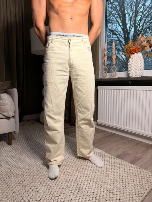 Woodbird raka jeans i ljus beige - Snygga ljusbeige jeans från Woodbird med klassisk femficksdesign och raka ben. Byxorna har normal passform och är tillverkade i mjukt bomullstyg. Perfekt för dig som gillar stilrena och neutrala färger.