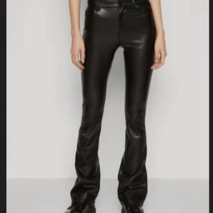 Svarta bootcut byxor i skinnimitation - Snygga svarta byxor i skinnimitation med bootcut-modell och låg/medel midja , Byxorna har dragkedja och knapp framtill samt en bootcut modell. Nedsydda så att de passar längre. Där de är uppsprättar nedtill, är de småhål (kom pv för bild) men de e inget man ser när man har på sig dem🥰