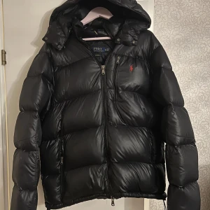Svart pufferjacka från Polo Ralph Lauren - Säljer en svart pufferjacka från Polo Ralph Lauren.  Stort eftertraktad jacka, i nyskick. Säljes pga för stor storlek, passar någon mellan 185 till 195