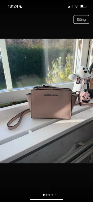 Ljusrosa axelväska från Michael Kors - BILDERNA ÄR IFRÅN MIN VINTED! Snygg ljusrosa axelväska från Michael Kors i stilren, boxig modell. Väskan har justerbar axelrem, silverfärgade metalldetaljer och dragkedja upptill. Tillverkad i strukturerat skinn med diskret logga framtill. Perfekt storlek för det viktigaste.