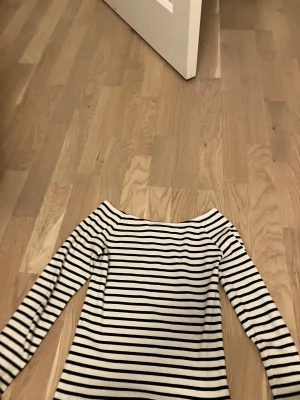 Randig långärmad tröja från LMTD - Snygg långärmad tröja från LMTD med svartvita ränder och ribbad struktur. Tröjan har en bred, båthalsad urringning och är figurnära i modellen. Perfekt för dig som gillar klassisk stil med en modern twist.