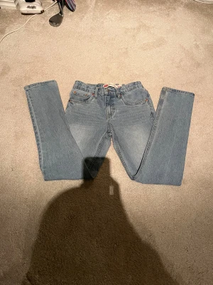 Levi's 512 ljusblå slim taper jeans i stl 12 år  - Ljusblå Levi's 512 jeans med slim taper passform. Klassisk femficksmodell med Levi's patch bak och röda detaljer vid bakfickan. Jeansen är tillverkade i bomullsdenim och har en smalare siluett som smalnar av vid ankeln. Oanvända 