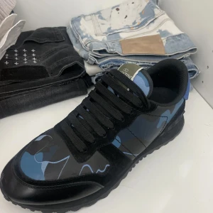 Valentino Rockrunner sneakers blå/svart - Säljer ett par Valentino Rockrunner sneakers med blått och svart camouflage-mönster. Skorna har platt sula, rund tå och svarta snören. Materialet är en mix av skinn och syntet, med coola detaljer och logga på plösen. Perfekt för dig som gillar streetstyle och exklusiva märken.        UTAN BOX !!!