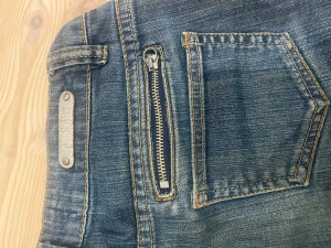 Blå jeansshorts med dragkedjor från Miss Sixty - Snygga blå jeansshorts från Miss Sixty med coola detaljer som dragkedjor på både fram- och baksidan samt dekorativa nitar. Klassisk femficksmodell med uppvikta ben och slitna effekter. Perfekt för dig som gillar streetstyle och vill sticka ut.