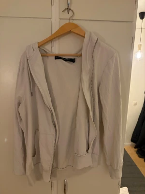 Ljusbeige hoodie med dragkedja - Säljer en ljusbeige hoodie från The Black Collection. Tröjan har huva med snörning, hel dragkedja framtill och två fickor. Tillverkad i mjuk bomull och har ribbade muddar vid ärmslut och nederkant. Perfekt för chill dagar.