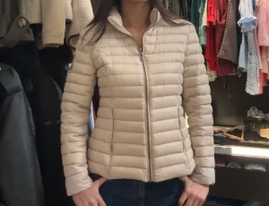 Beige pufferjacka med dragkedja - Säljer en beige pufferjacka med horisontella quiltade partier och hög krage. Jackan har en snygg, slim passform och stängs med dragkedja framtill. Perfekt för dig som vill ha en stilren och lätt jacka till kyliga dagar.