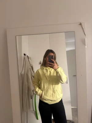 Gul hoodie med snörning - Säljer en ljusgul hoodie med snörning i huvan och stor magficka. Tröjan har en relaxed passform och är perfekt för dig som gillar en chill och enkel stil. Mjuk och skön, passar till jeans eller leggings.