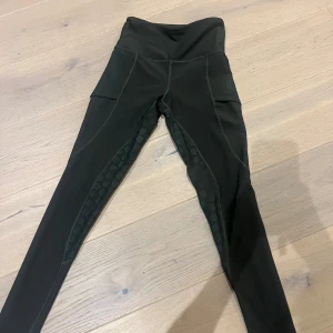 Svarta Maya Delorez ridleggings - Snygga gröna ridleggings från Maya Delorez med hög midja och smarta fickor på sidorna. Silikonmönster på insidan av benen ger extra grepp i sadeln. Stretchigt och bekvämt material som passar perfekt till ridning. 