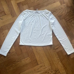Vit långärmad topp från H&M Divided - Säljer en enkel och stilren vit långärmad topp från H&M Divided. Modellen är rak med rundad hals och är tillverkad i mjuk stretchig polyesterblandning. Perfekt att styla med jeans eller kjol för en clean look.