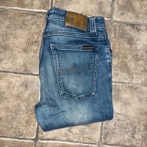 Nudie Jeans  - Snygga blå Tube Tom jeans från Nudie Jeans med klassisk femficksdesign och subtila slitningar. Jeansen är tillverkade av 98% ekologisk bomull och 2% elastan för skön stretch. Midja 37cm, längd 99cm. Ifall det inte finns någon bild i annonsen där jag bär plagget så är det för att jag ej kan ha storleken heller passformen, så kolla måtten för storlek och googla på modellnamnet för passform 😉S4