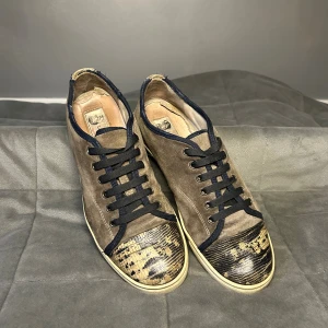 Lanvin sneakers  - Lanvin-sneakers till salu. Modell med unik tå- och hälpanel i reptilmönstrat läder. Överdelen i mjuk mocka med mörka detaljer. Skorna är äkta och i gott begagnat skick. Originalkartong ingår och är i bra skick.  • Nypris: 3 995 kr • Storlek: EU 40 (innersula ca 27 cm)