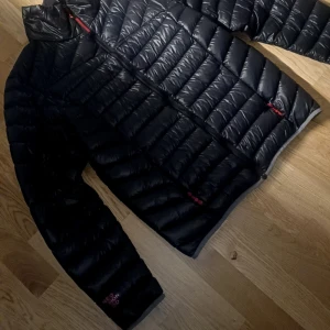 Svart dunjacka från Neo Mondo riktigt fin jacka  - Snygg svart dunjacka från Neo Mondo i storlek L. Jackan har quiltad design, röda detaljer vid dragkedjorna och hög krage. Materialet är glansigt och lätt, perfekt för kalla dagar. Jackan har långa ärmar och två sidofickor med dragkedja. Storlek L men passar medium också  