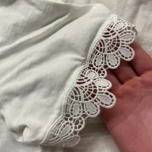 Vit t-shirt med spets från Zara - Vit t-shirt från Zara med v-ringning och korta ärmar. Ärmsluten har snygga spetsdetaljer som ger en extra touch. Tillverkad i mjuk bomull, perfekt för dig som gillar stilrena plagg med lite extra detaljer.