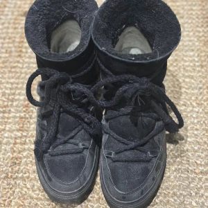 Svarta Inuikii vinterskor - Säljer ett par svarta Moon Boots från Inuikii med grova snören och rund tå. Skorna har en kombination av mocka och skinn, samt en platt sula. Perfekta för vintern med sin höga och fodrade design som håller fötterna varma.