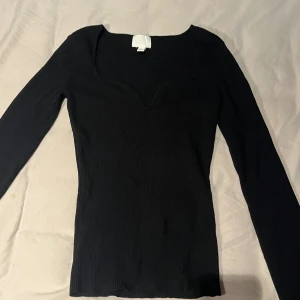 Långärmad topp H&M - Svart ribbad topp från H&M med lång ärm och snygg v-ringad halsringning. Modellen är figurnära och har en stilren, enkel design som funkar till många olika looks. Materialet är mjukt och stretchigt för en bekväm passform. Använd väldigt lite