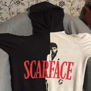 Scarface hoodie  - Säljer en riktigt snygg hoodie med Scarface-tryck. Tröjan är delad i svart och vitt med stor röd Scarface-text och ikoniskt motiv framtill. Säljer då tröjan blivit liten för mig. 44 cm i midjan och 14 cm axel. 