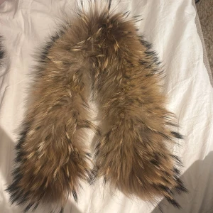 Päls - Säljer en fluffig avtagbar päls för jackor i brun med svarta toppar. Pälsen har en bred och rundad form med knappar på insidan för enkel fastsättning.