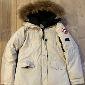 Vit dunjacka från Canada Goose - Säljer en beige Canada Goose dunjacka med fluffig päls på huvan och svart innerfoder i storlek XS. Jackan har en defekt på vänstra fickan och på dragkedjan därmed priset. Vid stort intresse kan jag gå ner i pris👍 Vid mer frågor hör bara ev er! Fraktas inom 24h✅