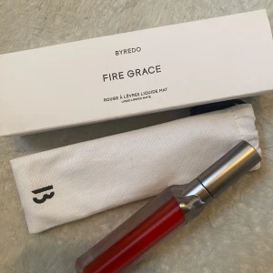 Byredo Fire Grace flytande läppstift - Säljer ett Byredo Fire Grace flytande läppstift i en intensiv röd nyans med matt finish. Kommer i snygg metallhylsa och med originalförpackning samt vit tygpåse. Perfekt för dig som vill ha en statement-läpp. Endast öppnad för att se färgen. Oanvänd 