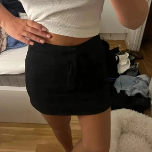 Svart kortkjol med snörning - Snygg svart kortkjol med snörning framtill. Kjolen har en enkel och stilren design med rak passform som sitter normalt. Perfekt att matcha med en croppad topp eller hoodie för en chill look. Egensydd 