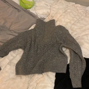 Grå stickad tröja  - Mysig grå stickad tröja från BikBok i storlek XS. Tröjan har hög krage med half zip-dragkedja och kabelstickat mönster på ärmarna. Supervarm och gosig. 