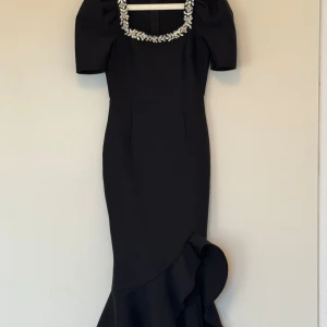 Svart långklänning med strassdetaljer - Supersnygg svart långklänning med puffiga korta ärmar och fyrkantig halsringning dekorerad med glittrande strassblommor. Passar både S och M