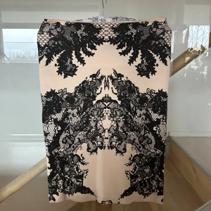 Beige kjol med svart spetsmönster McQueen - Supersnygg beige kjol från Alexander McQueen med ett detaljerat svart spetsmönster som ger en lyxig och edgy vibe. Kjolen är rak i modellen och har en midilängd som passar perfekt till sneakers eller boots. Materialet känns mjukt och följsamt mot huden.