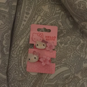 Hello Kitty rosa örhängen med blomma - Supergulliga rosa örhängen från Hello Kitty med motiv av Hello Kittys ansikte och en glittrig rosett. Varje örhänge har även en rosa blomma bredvid. Perfekt för dig som älskar söta accessoarer och Hello Kitty!