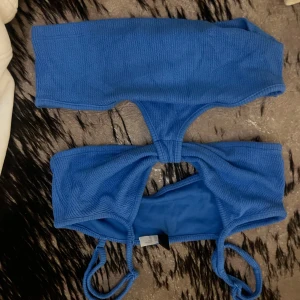 Blå bikini med ribbad struktur - Snygg blå bikini med ribbad struktur och twistad detalj framtill. Toppen har smala axelband och en modern, enkel design som känns både trendig och bekväm. Perfekt för strandhäng eller poolparty i sommar.