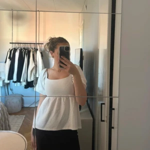 Vit blus med puffärm och knyt i ryggen - Supersöt vit blus med puffiga korta ärmar, fyrkantig ringning och öppen rygg med dubbla knytband. Blusen har en lätt strukturerad bomullskänsla och faller fint över kroppen. Perfekt för dig som gillar romantiska detaljer och en luftig look.