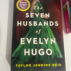 The Seven Husbands of Evelyn Hugo - En bok med en glamorös kvinna i en grön klänning på omslaget, vilket ger vibbar av Hollywood och dramatik. Perfekt för dig som gillar berättelser om kändisskap, relationer och hemligheter. En modern klassiker som har blivit populär bland unga vuxna.