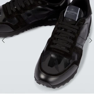 Valentino Garavani Rockrunner sneakers - Svarta Valentino Garavani Rockrunner sneakers med coolt kamouflagemönster, snörning och platt sula. Skorna har detaljer i både skinn och mocka samt nitar på hälen för extra edge. Perfekt för dig som gillar stilrena och unika sneakers.