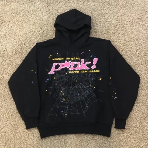 Svart hoodie från Pink! med tryck - Svart hoodie från Pink! med färgglatt tryck på bröstet, text och spindelnätsmotiv samt små stjärnor i gult, blått och lila. Tröjan har huva och långa ärmar, perfekt för dig som gillar coola och unika prints.