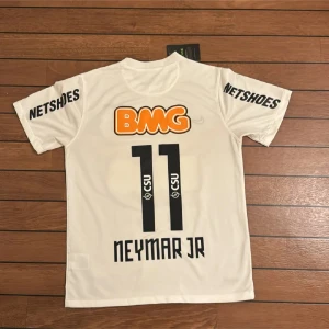 Vit Santos Neymar Jr fotbollströja Nike - Säljer en officiell Santos fotbollströja från Nike i storlek S, med Neymar Jr och nummer 11 på ryggen. Tröjan är vit med svarta och orange tryck, korta ärmar och Dri-Fit material. Klubbmärke och sponsorer på bröstet och ärmarna. Perfekt för dig som älskar brasiliansk fotboll.