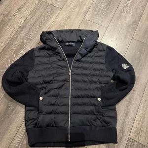 Mörkblå grisch cardigan från La’Santino - Snygg mörkblå cardigan från La’Santino med stickade ärmar och huva. Jackan har quiltad framsida, två fickor med tryckknappar och dragkedja hela vägen. Märkespatch på vänster ärm och ribbade muddar. Perfekt för dig som gillar stilren och väldigt ”grisch” look. Nypris 125€. Jackan är helt oanvänd och kommer i original packetering och en rabbatkod på 20% på la’Santinos hemsida följer med🤫 Är  185cm och ca 85kg och jackan sitter jättebra på mig👍